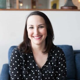 smiling woman in a black and white polka dot shirt with short dark hair sitting in a blue chair