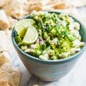 fish ceviche verde - fish ceviche topped with jalapenos and limes in a blue bowl on a marble slab surrounded by tortilla chips