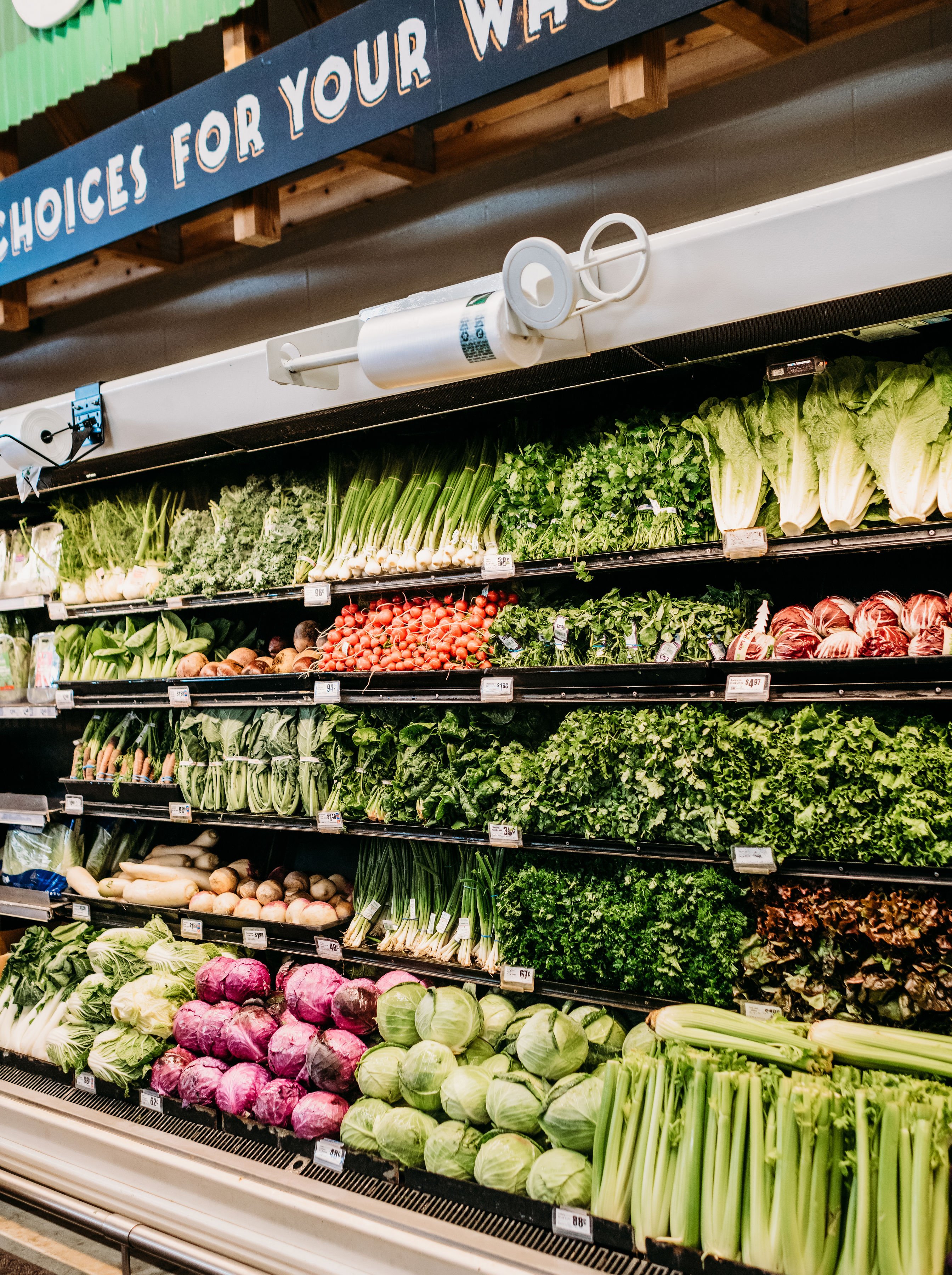 grocery store produce aisle filled with green veggies, pruple cabbage, and carrots