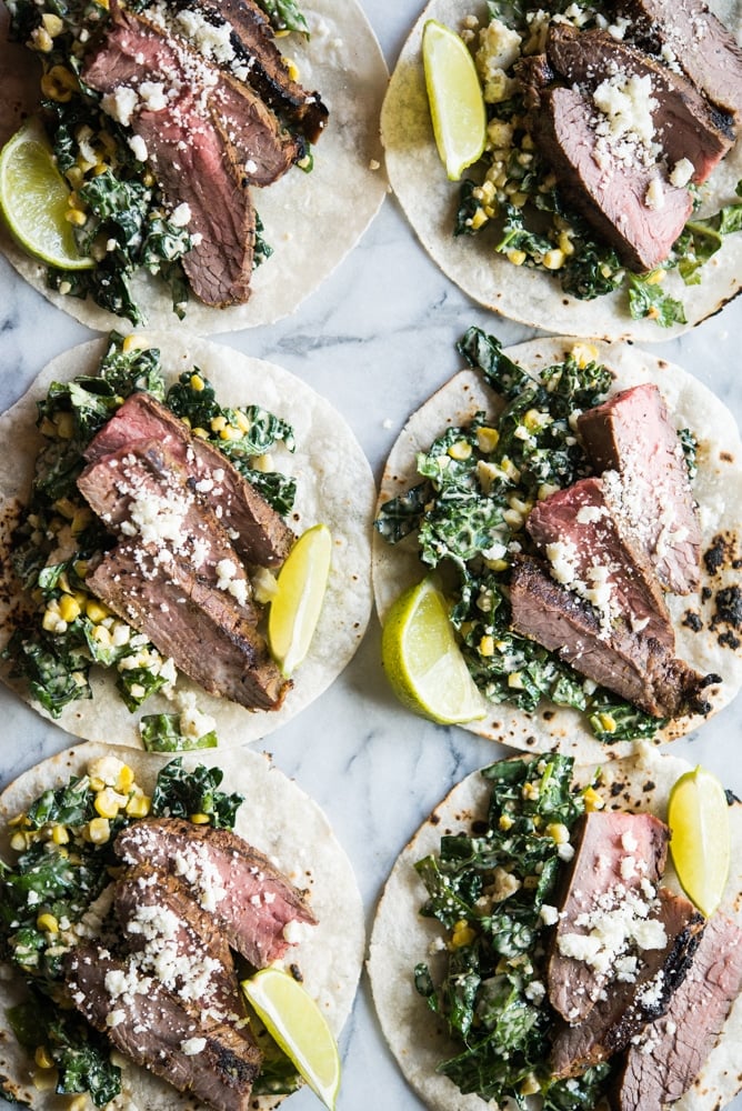 beef carne asada on top of kale and slaw in a corn tortilla on a marble board