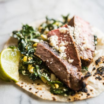 beef carne asada on top of kale and slaw in a corn tortilla on a marble board