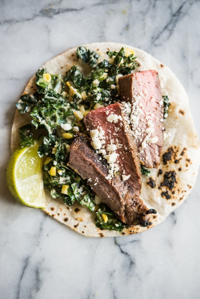 beef carne asada on top of kale and slaw in a corn tortilla on a marble board