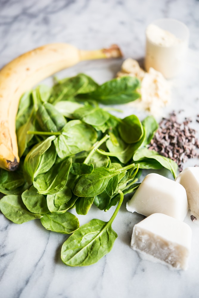ingredients for mint chocolate chip green smoothie packs - banana, spinach, protein powder, cacao nibs, and coconut milk ice cubes