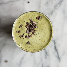 green mint chocolate chip protein smoothie in a glass on a marbale board