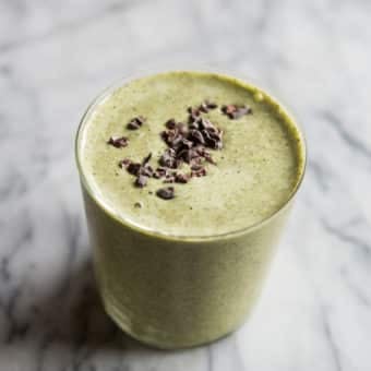 green mint chocolate chip protein smoothie in a glass on a marble board