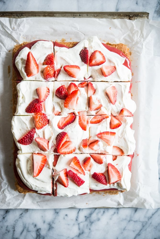 Strawberry shortcake - Vanilla sheet cake topped with whipped cream and strawberries on parchment paper on a marble slab.