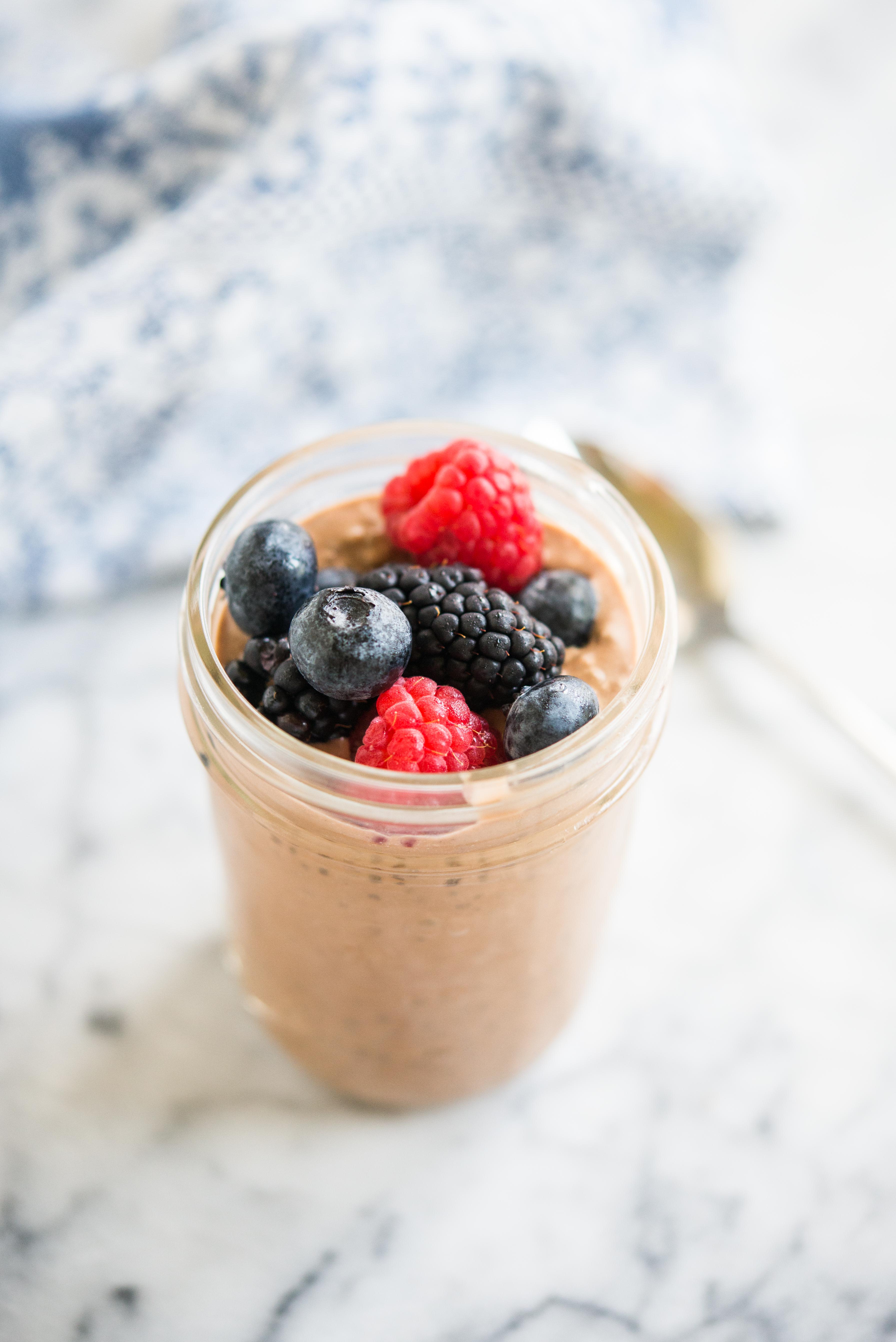 chocolate chia pudding in a mason jar topped with berries on a marble board with a spoon and blue towel