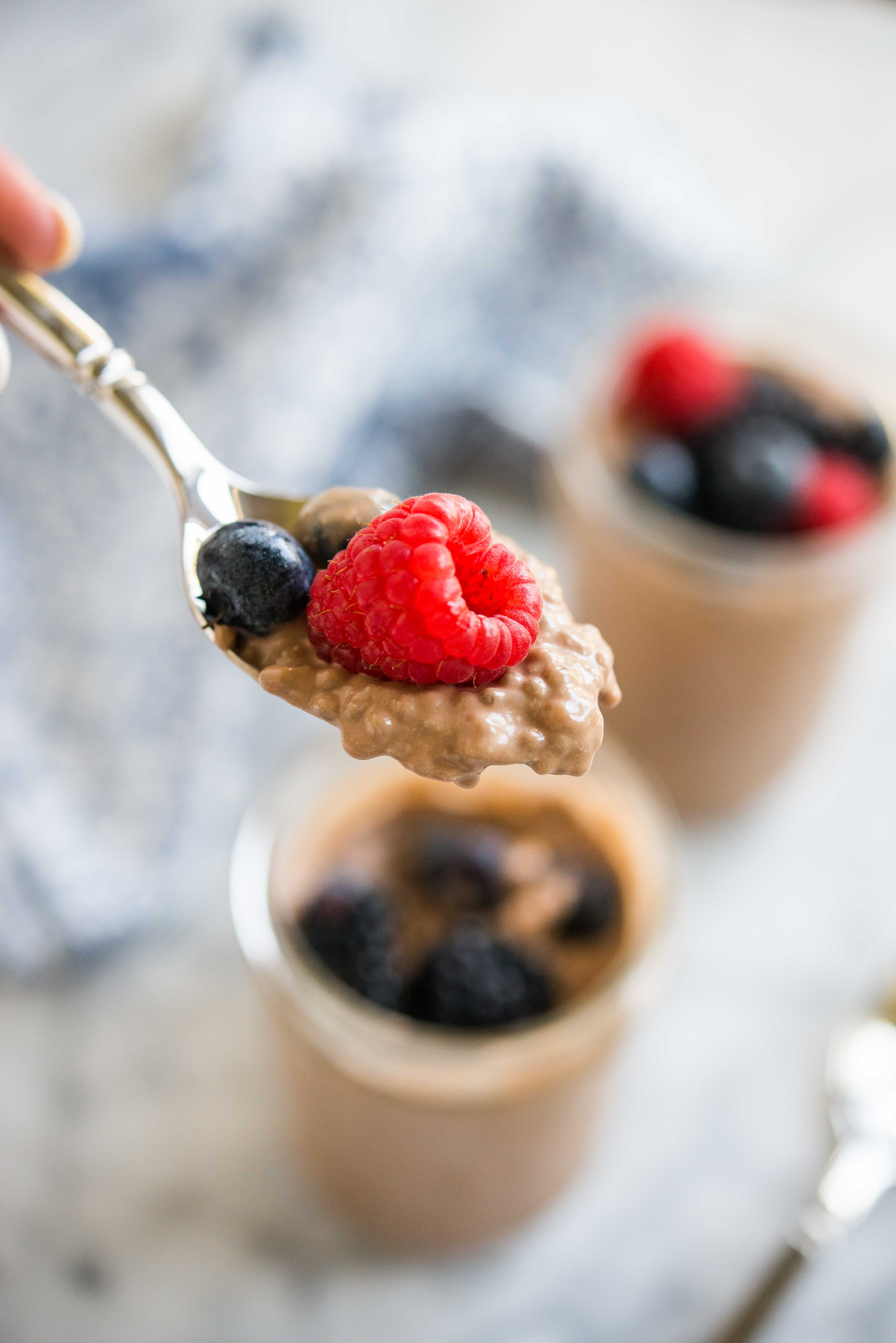 spoonful of chocolate chia pudding with a raspberry and two blueberries on top