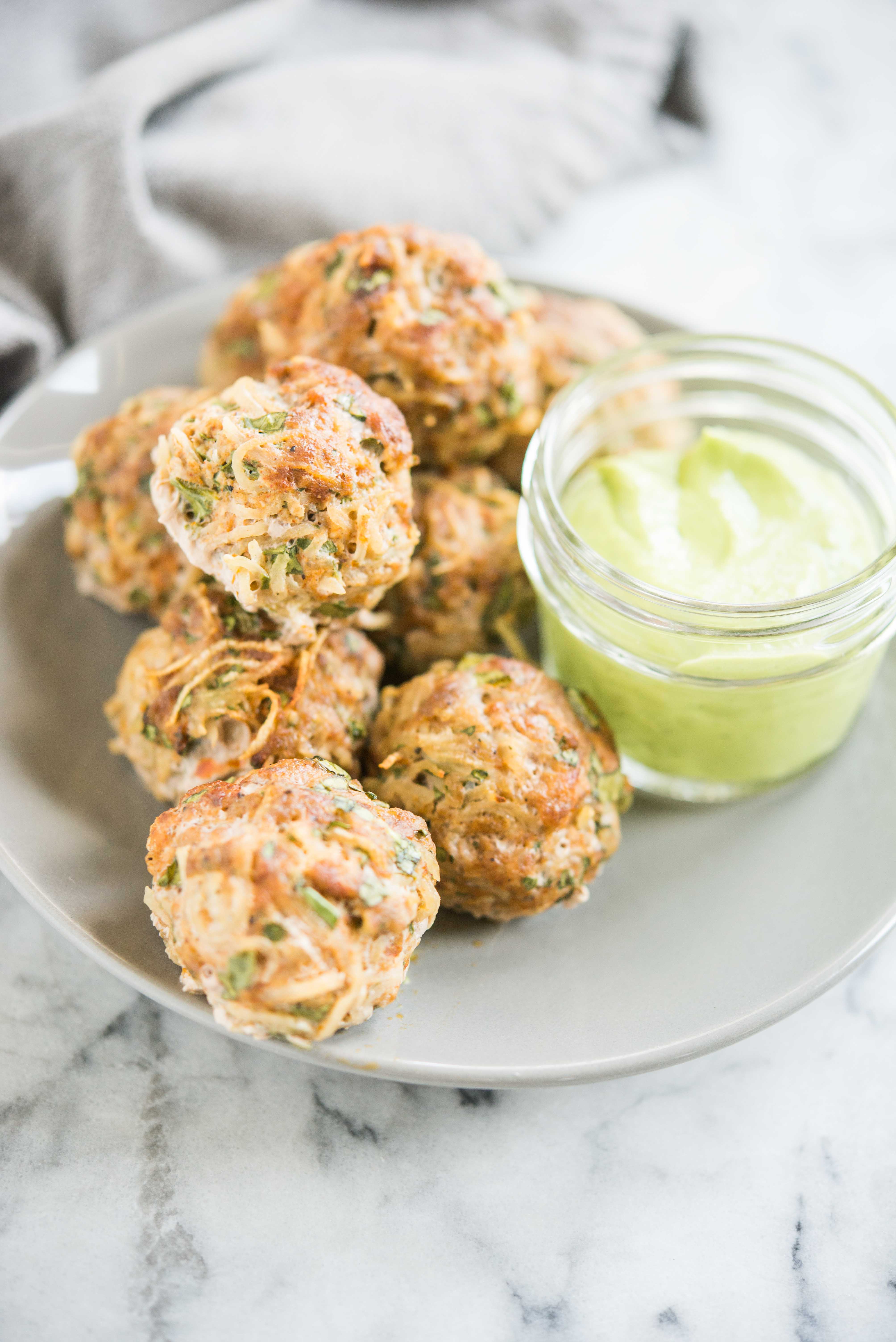 chorizo and potato breakfast meatballs on a grey plate sitting next to a glass jar of creamy green sauce on a marble board