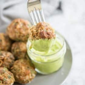 fork holding a chorizo potato breakfast meatball dipped in a bright green sauce