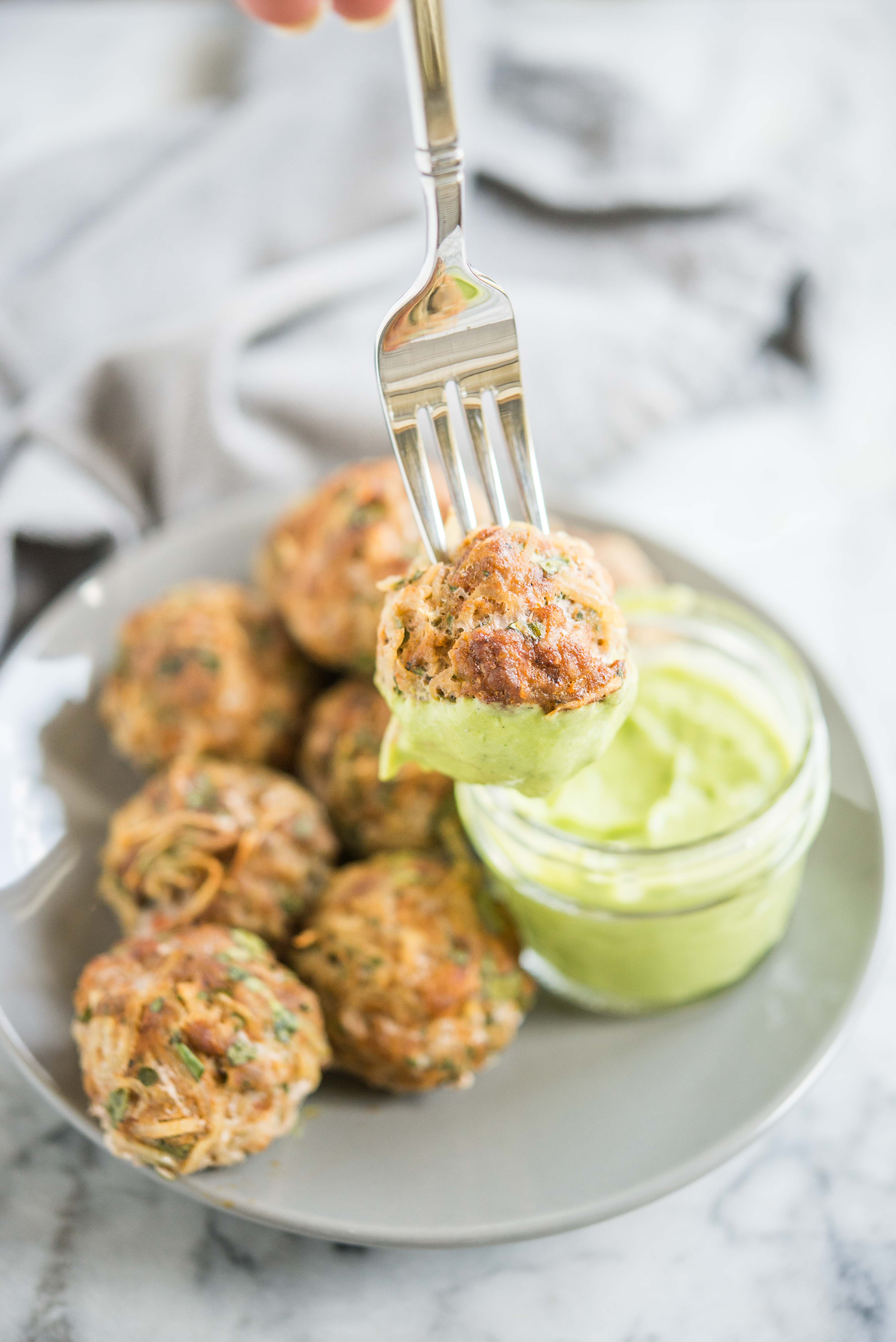 fork holding a chorizo potato breakfast meatball dipped in a bright green sauce 