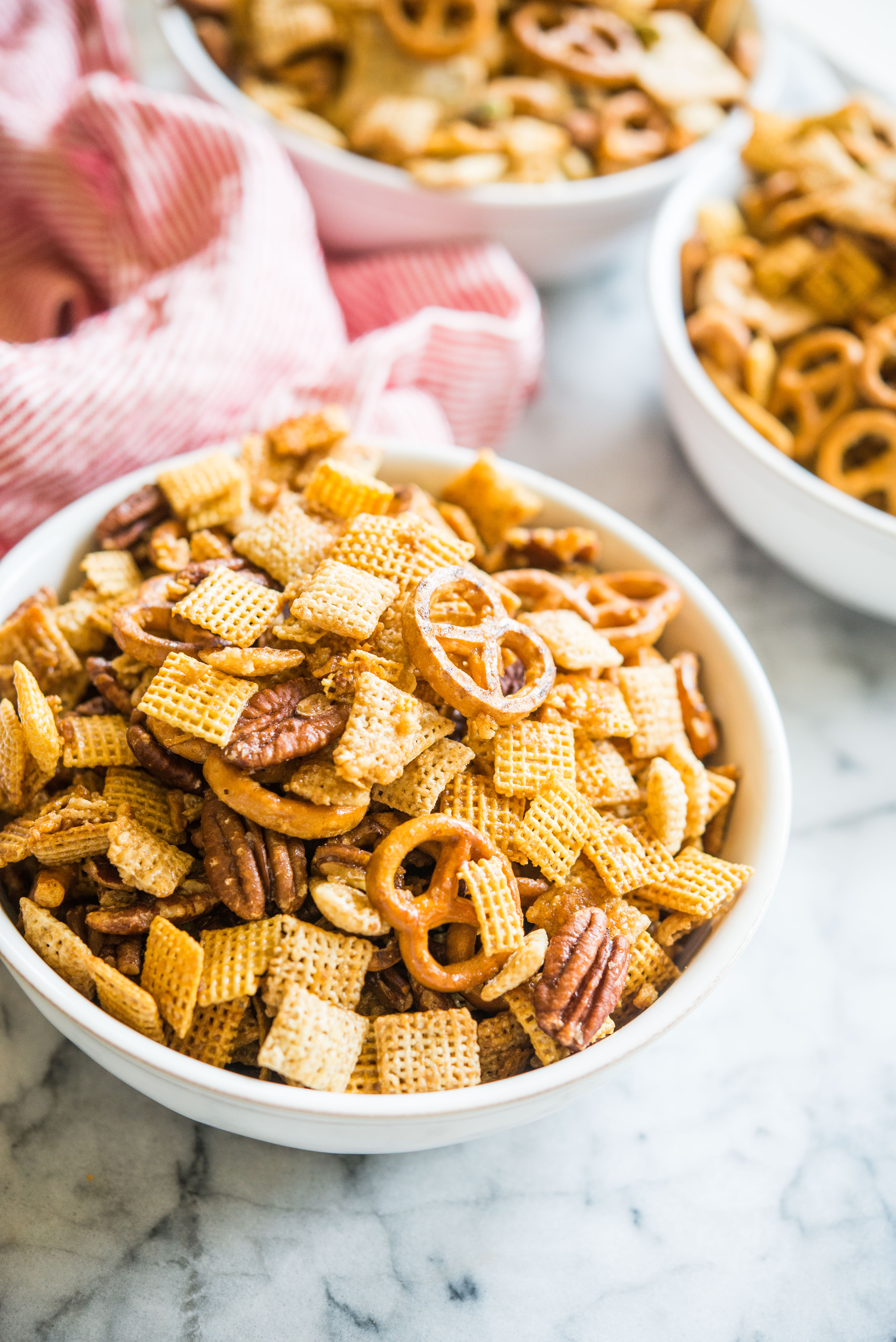 gluten free chex mix in a bowl on a marble board with a red and white striped napkin sitting behind it
