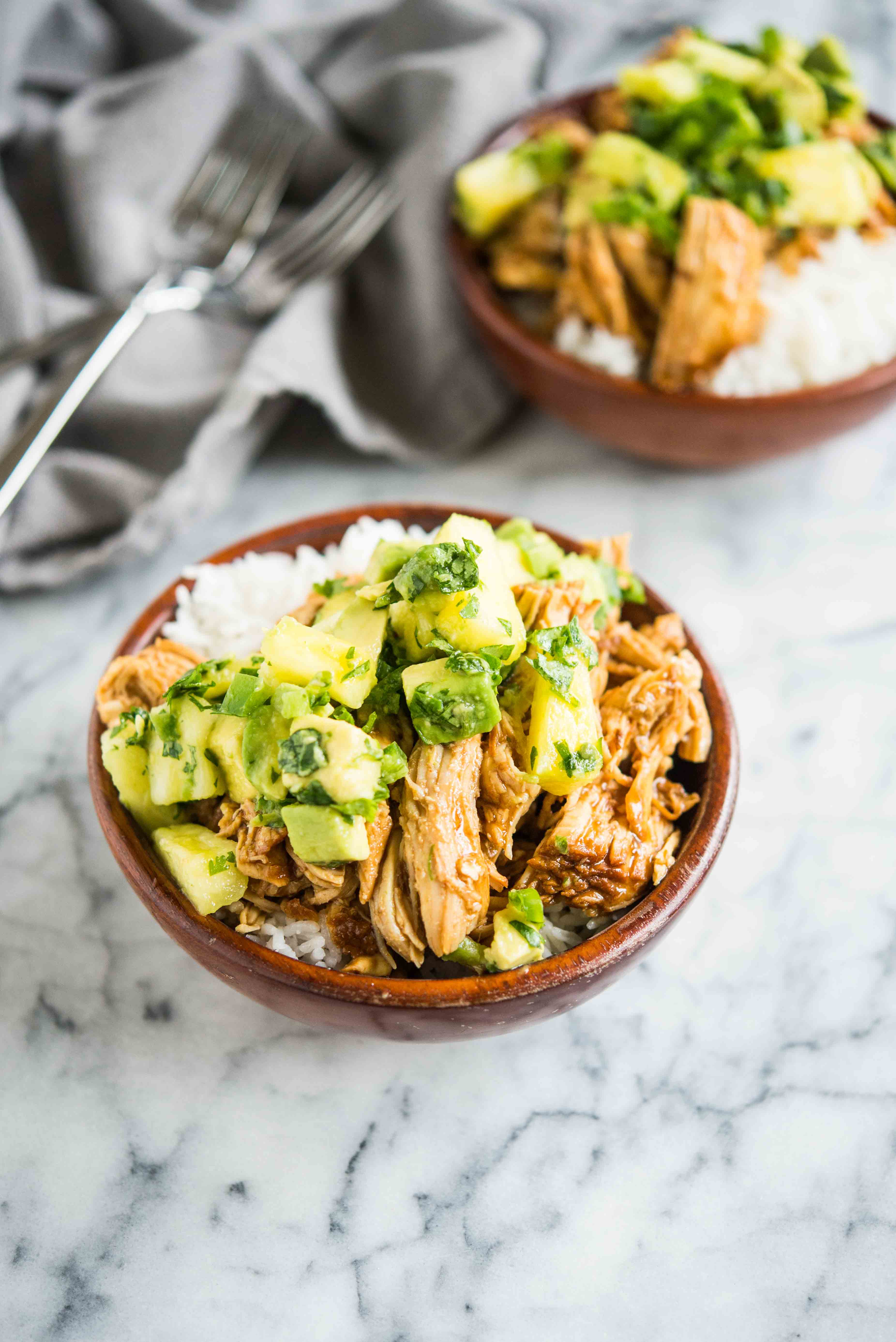wooden bowls filled with white rice topped with island chicken and pineapple avocado salsa on a marble board