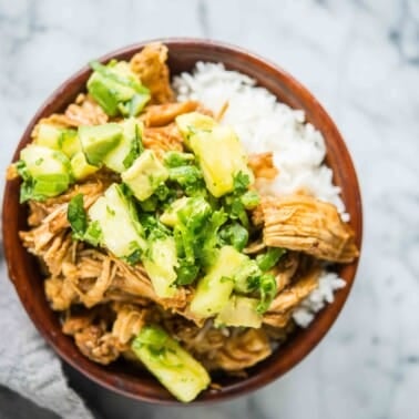 instant pot hawaiian chicken bowls - shredded chicken in a brown sauce over white rice topped with pineapple and avocado salsa and garnished with cilantro