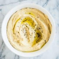 hummus topped with cracked black pepper in a white bowl on a marble board