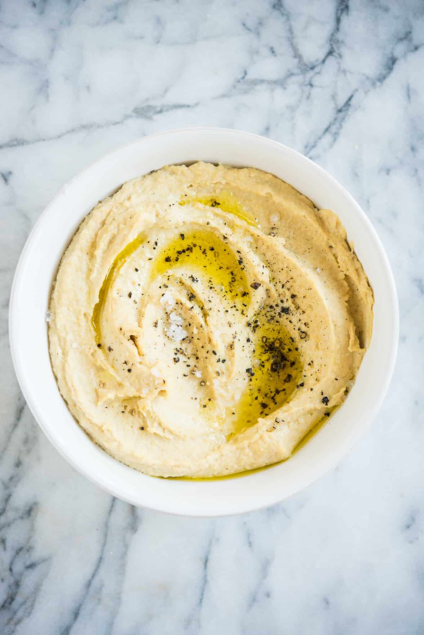hummus topped with cracked black pepper in a white bowl on a marble board