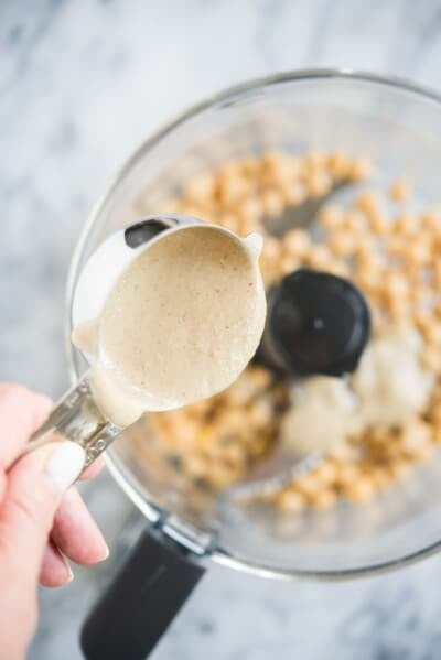 how to make hummus - tahini being poured into a food processor filled with chickpeas