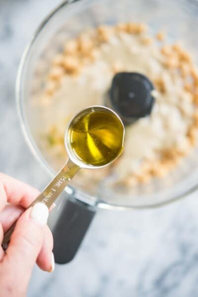 how to make hummus - olive oil being poured into a food processor with chickpeas