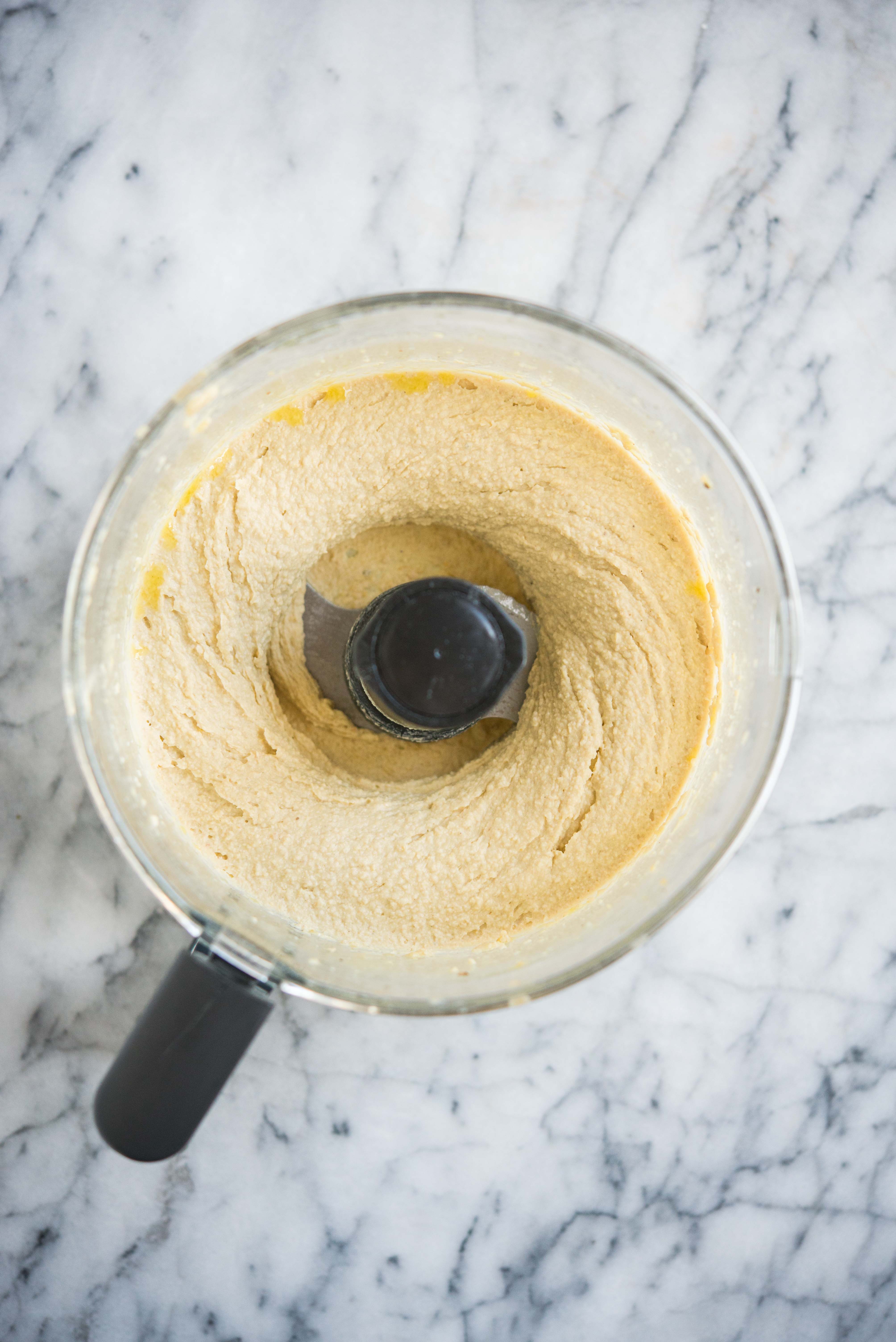 how to make hummus - hummus in a food processor on a marble surface