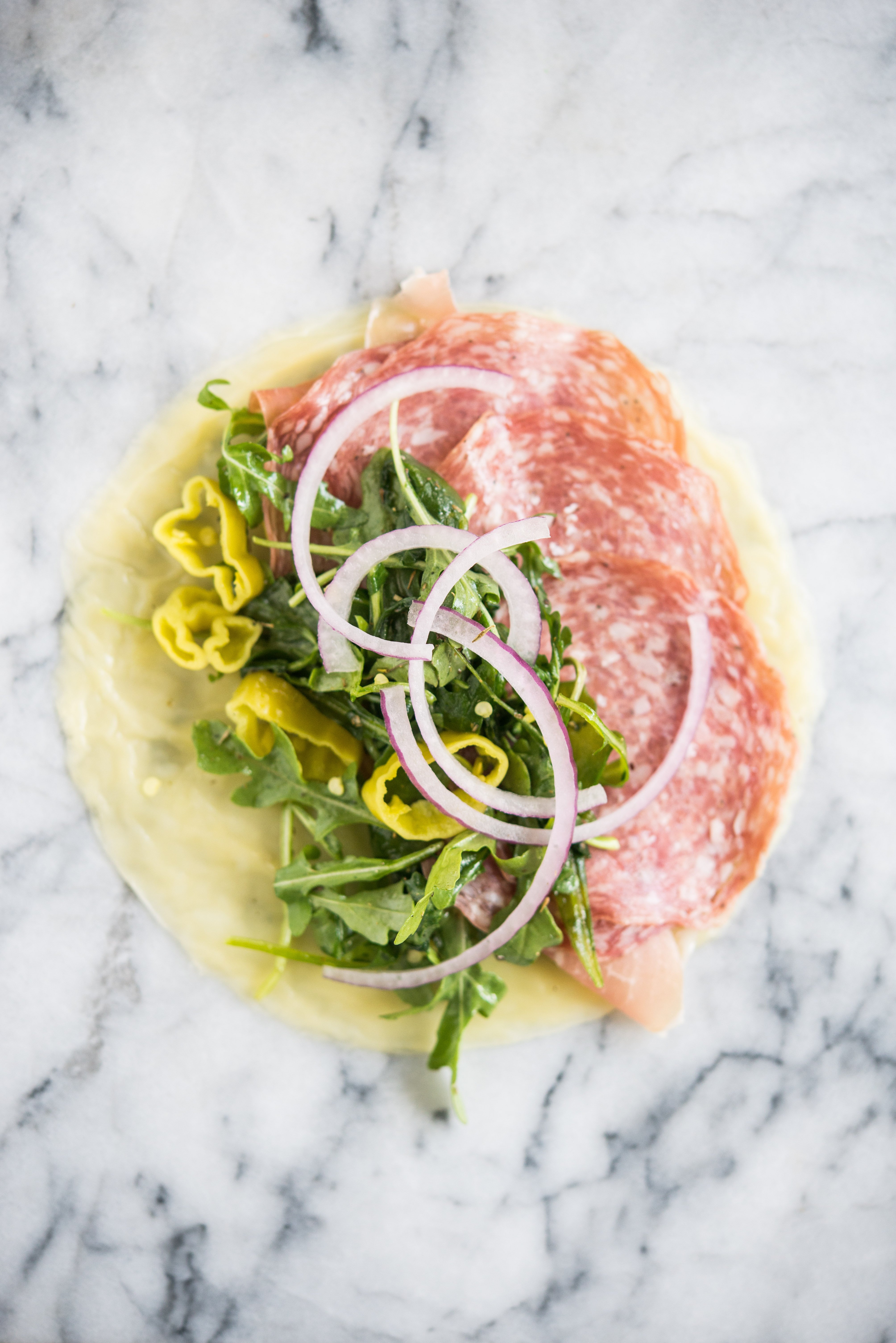 italian lunch meats, arugula, red onions, pepperonicini on a cheese wrap on a marble board