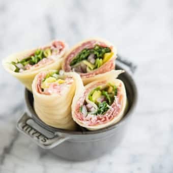 Keto Lunch wraps with Italian meats, arugula, pepperoncini, and red onion, cut in half in a small grey bowl on a marble board