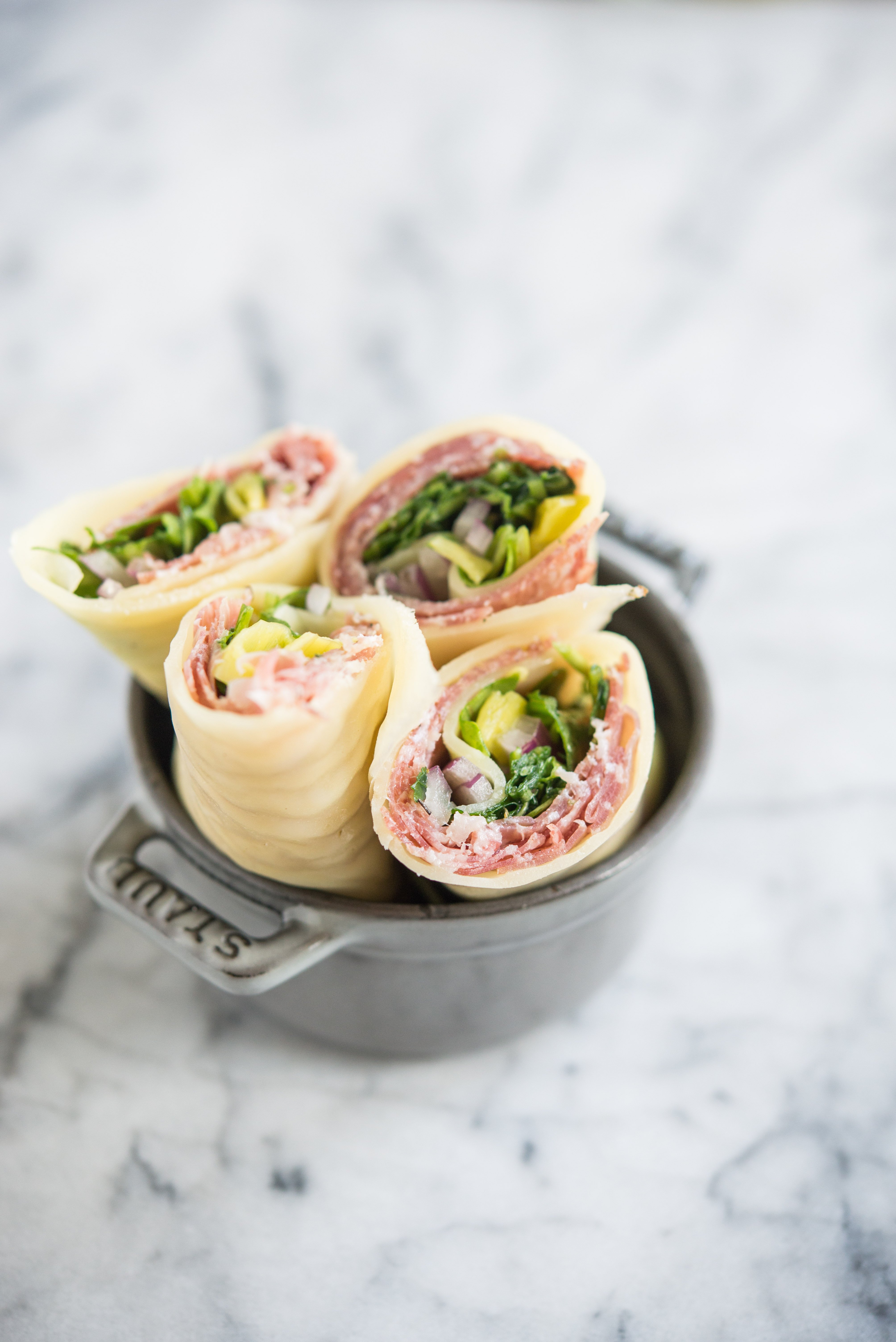 Keto Lunch wraps with Italian meats, arugula, pepperoncini, and red onion, cut in half in a small grey bowl on a marble board