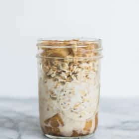 apple cinnamon overnight oats in a mason jar against a white wall sitting on a marble countertop