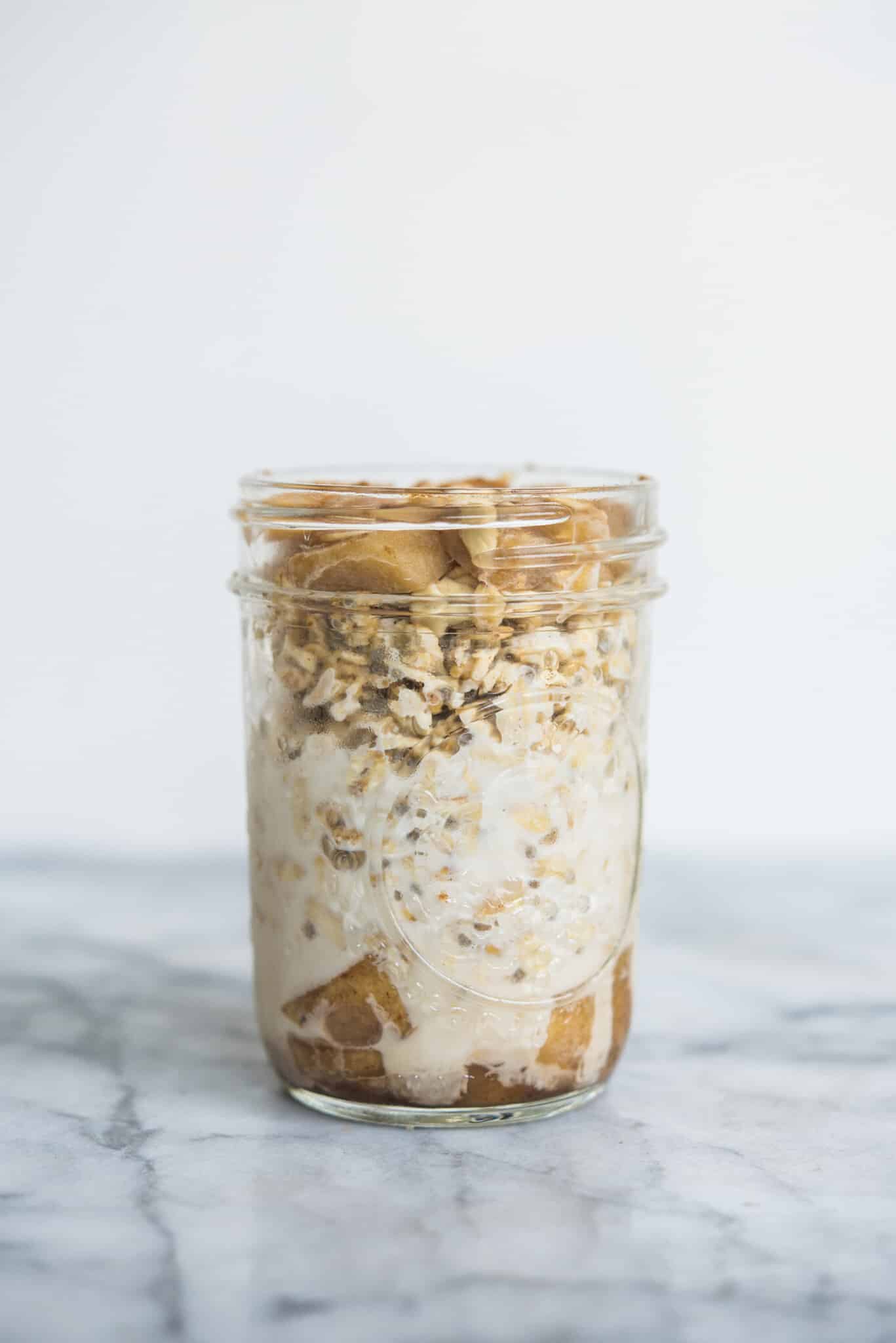 apple cinnamon overnight oats in a mason jar against a white wall sitting on a marble countertop