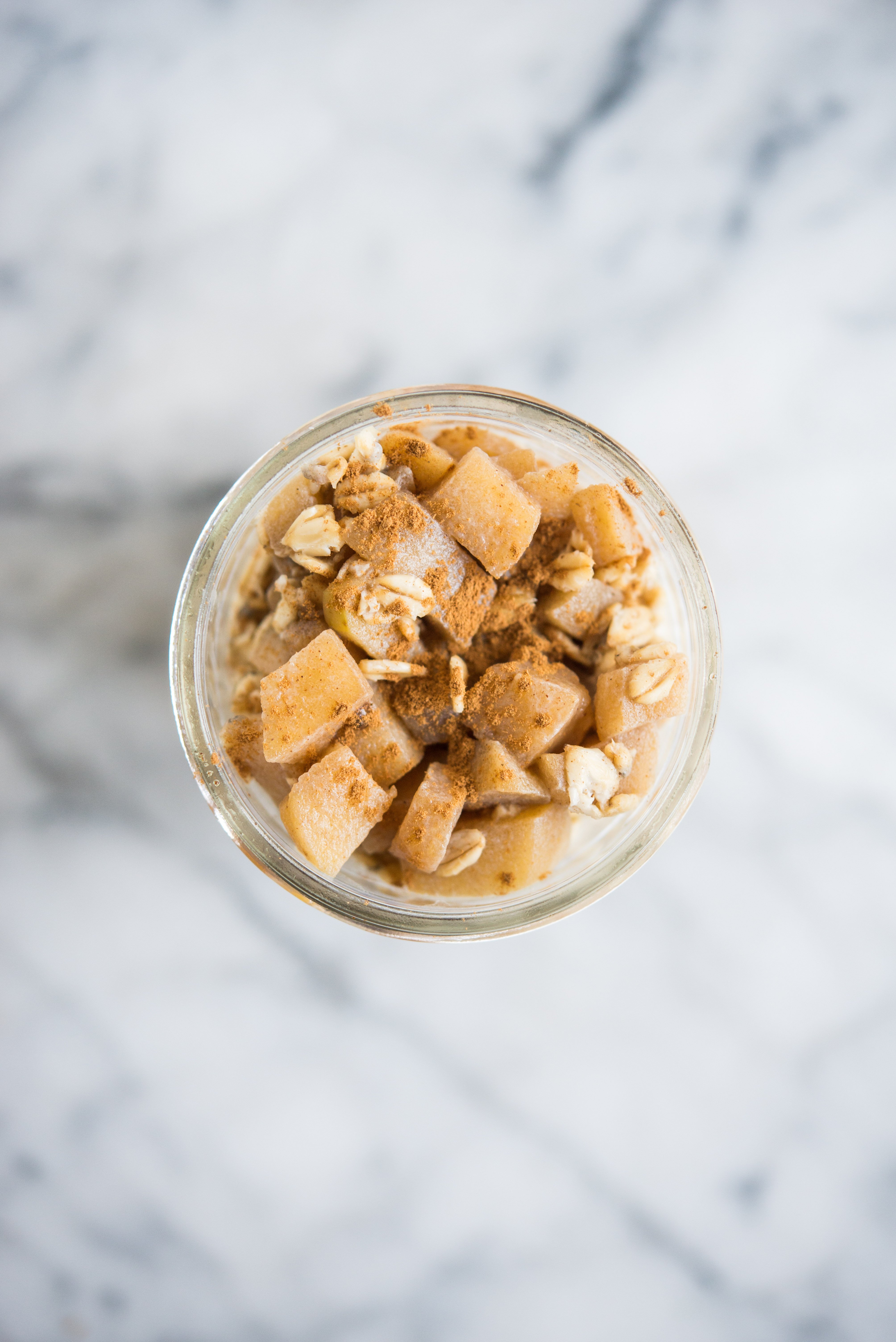 overnight oats topped with apples and cinnamon in a mason jar sitting on a marble countertop