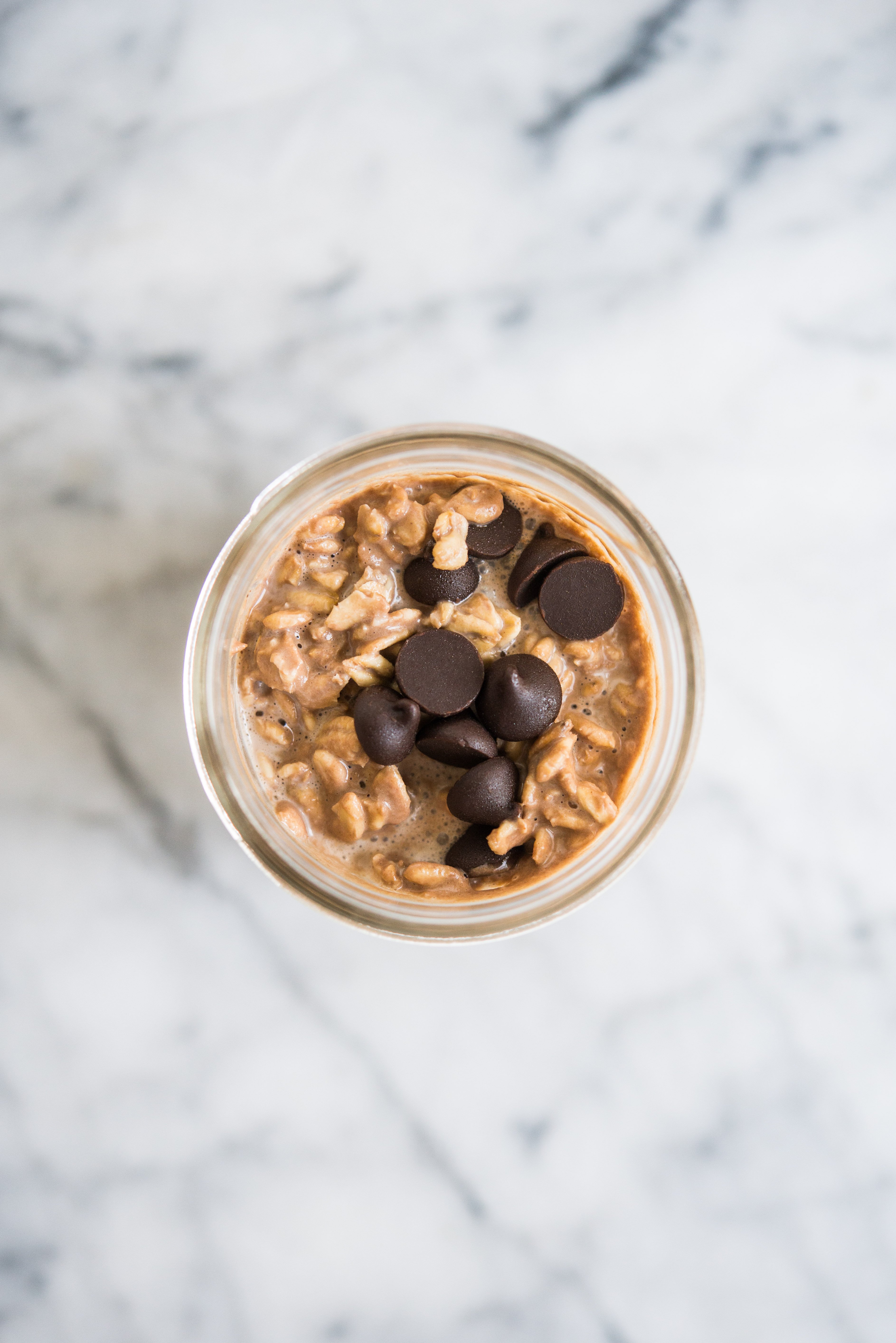 chocolate peanut butter overnight oats topped with chocolate chips in a mason jar sitting on a marble counter