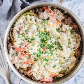 keto philly cheesesteak skillet - ground beef, peppers, and onions covered with provolone cheese and garnished with parsley on a marble board