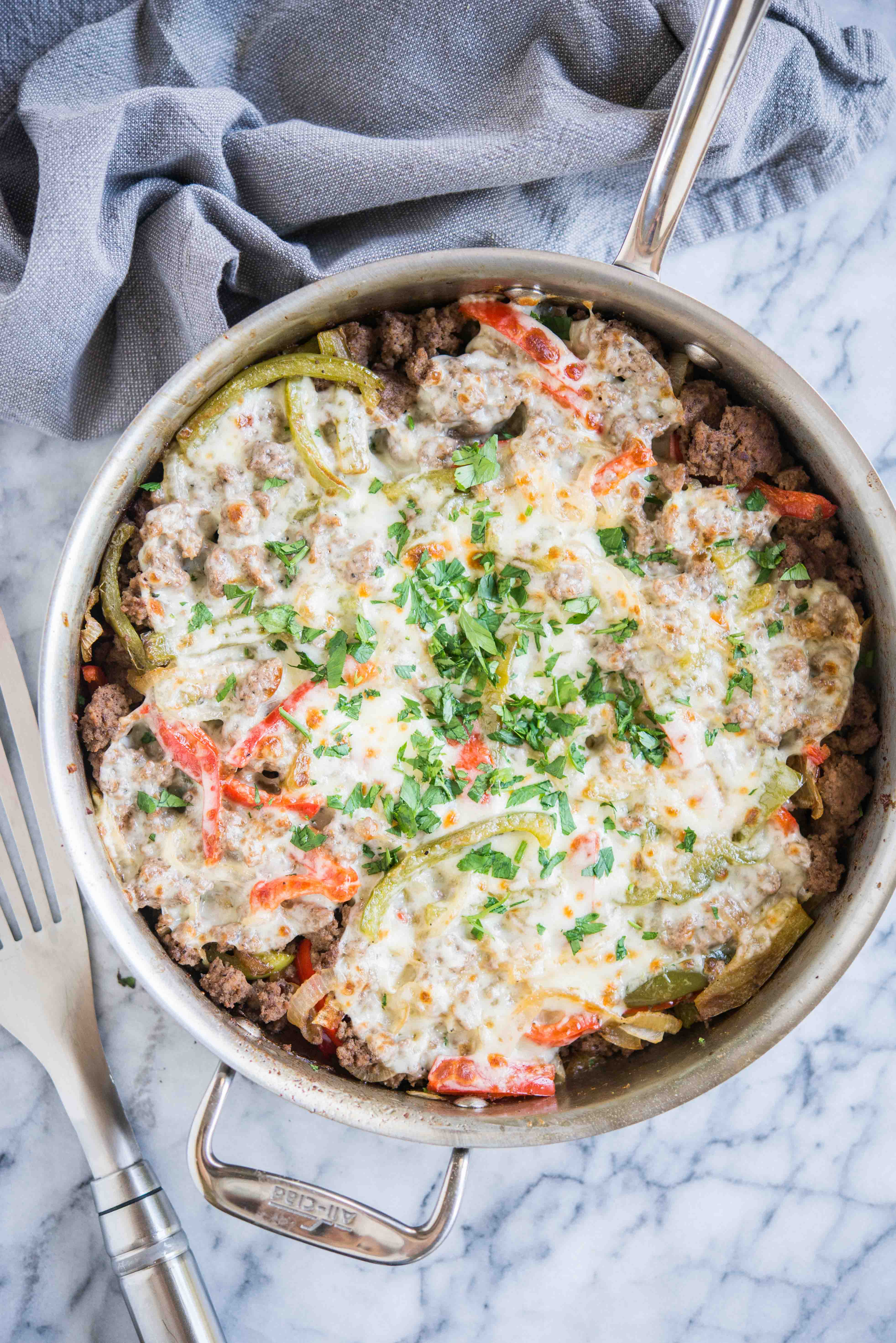 keto philly cheesesteak skillet - ground beef, peppers, and onions covered with provolone cheese and garnished with parsley on a marble board