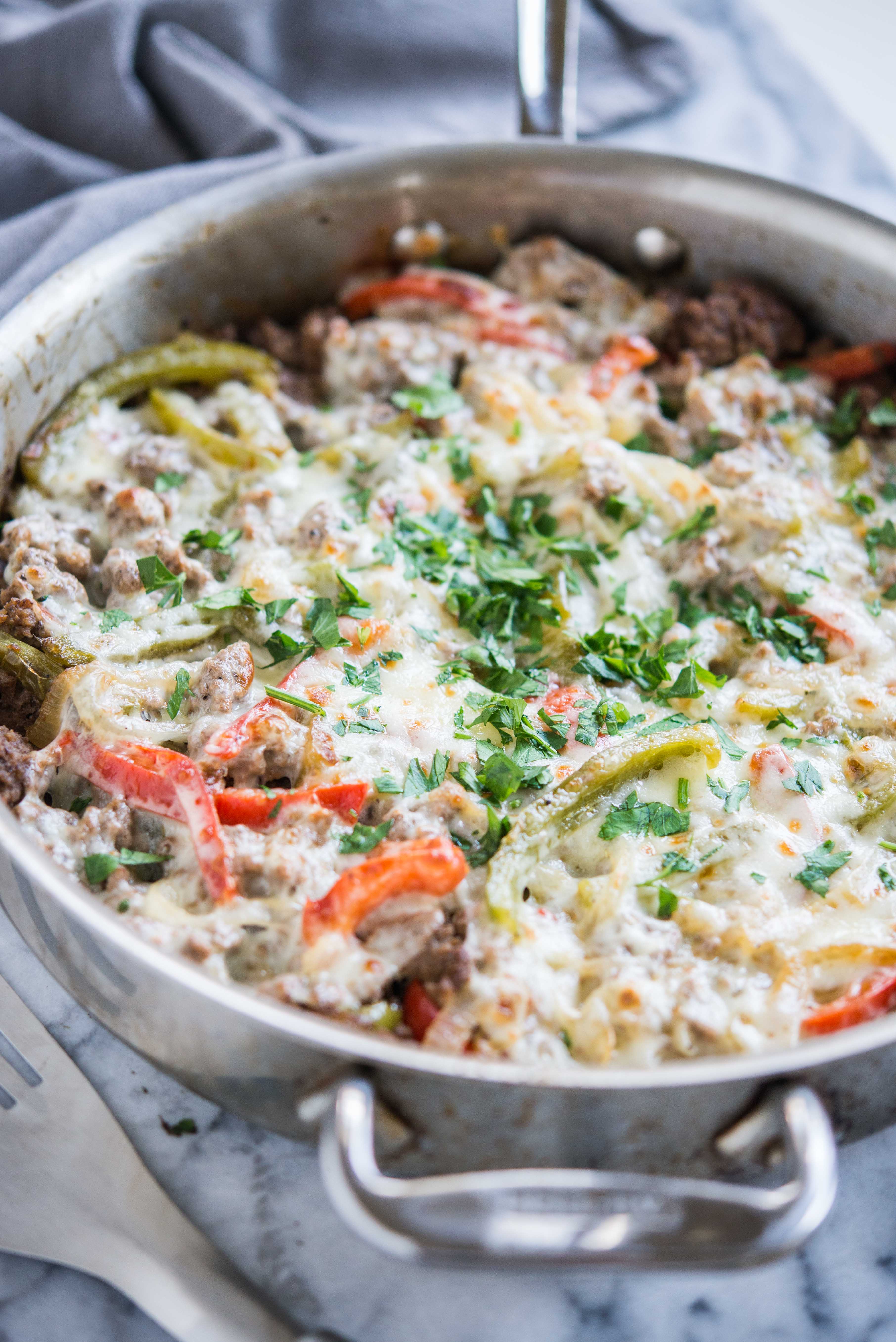 keto philly cheesesteak skillet - ground beef, peppers, and onions covered with provolone cheese and garnished with parsley on a marble board