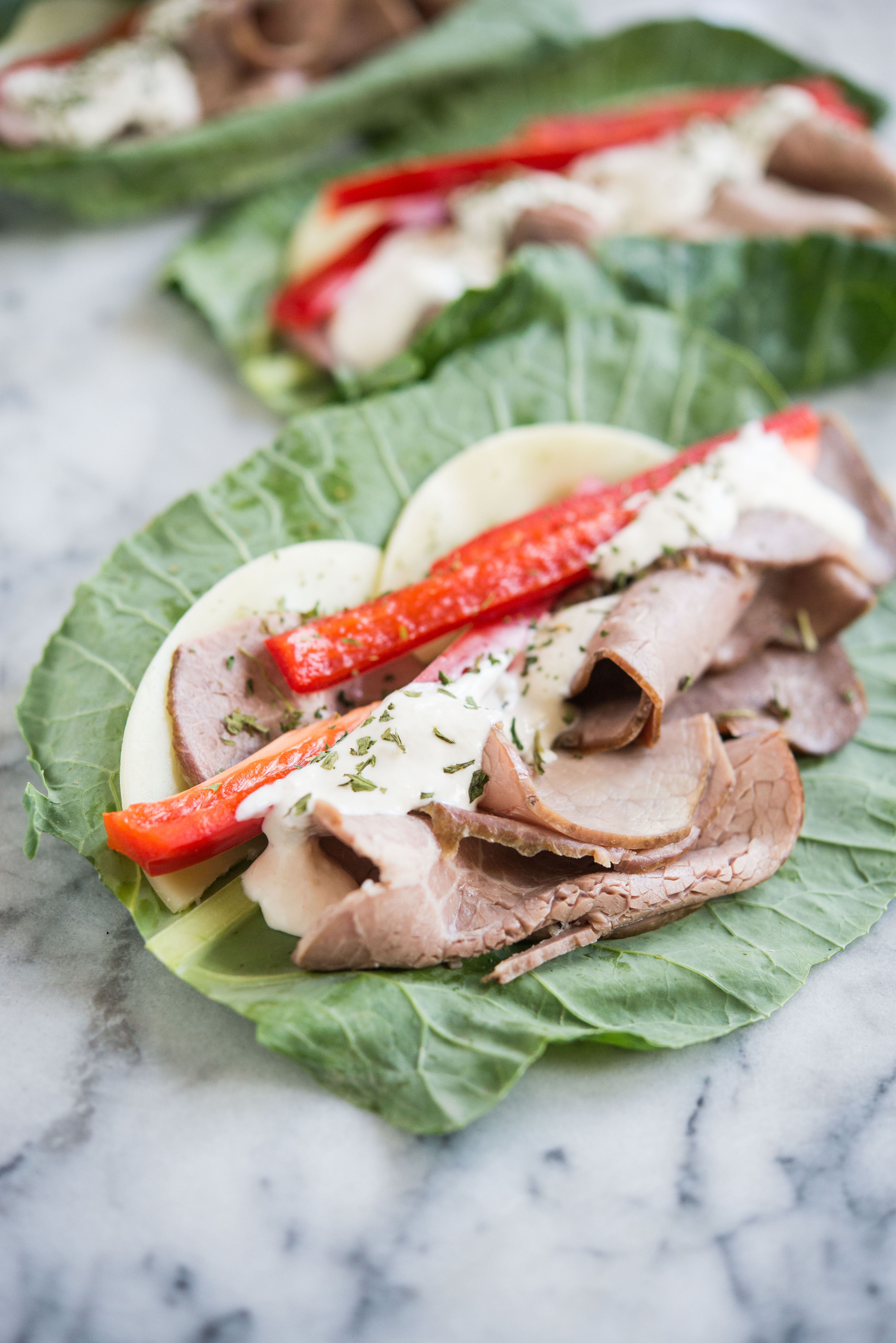 low carb roast beef wraps - collard green leaves layered with provolone cheese, roast beef, red bell peppers, and horseradish sauce sitting on a marble board