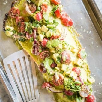 salmon topped with cilantro lime sauce and tomato avocado salsa on a baking sheet on a marble board