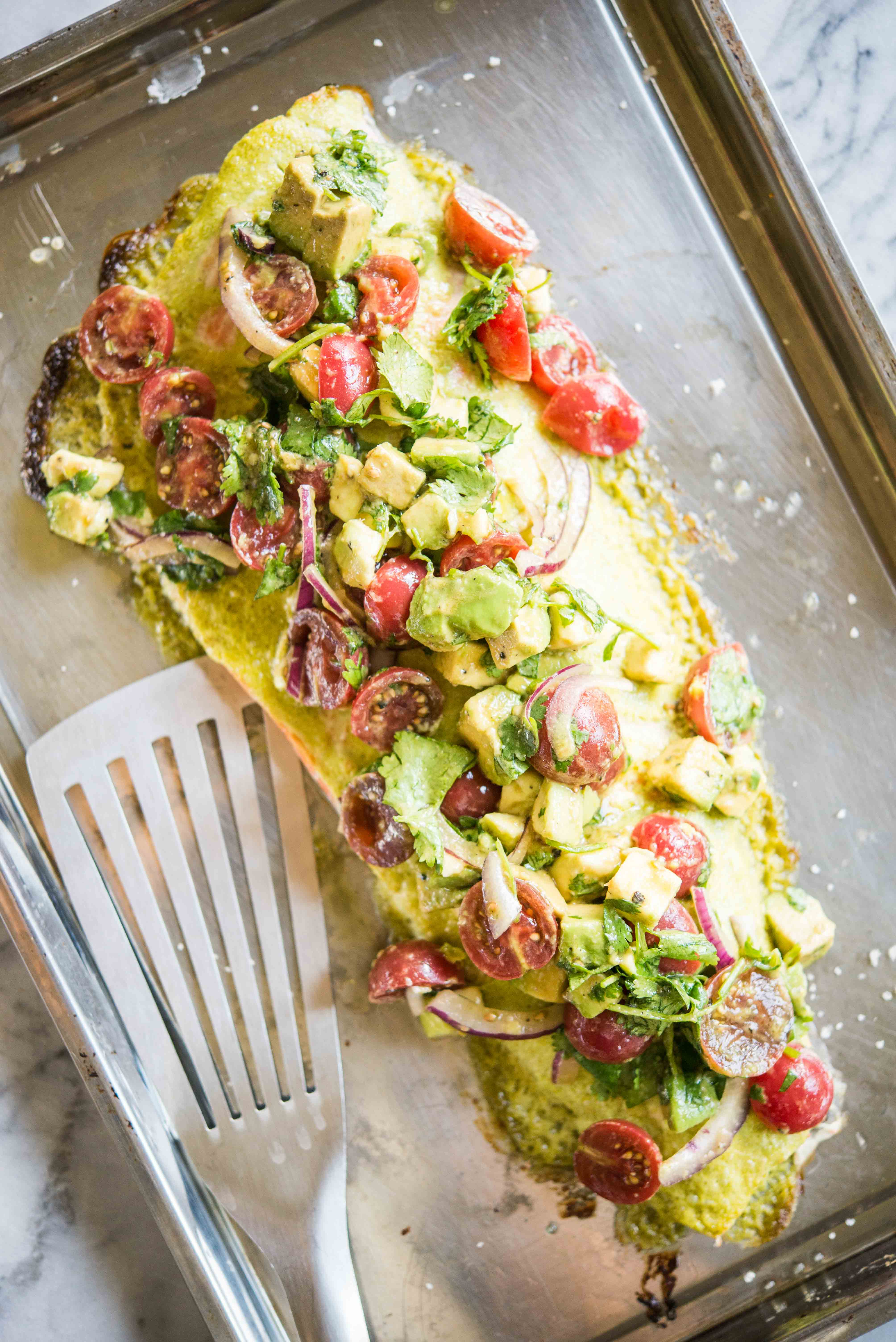 salmon topped with cilantro lime sauce and tomato avocado salsa on a baking sheet on a marble board