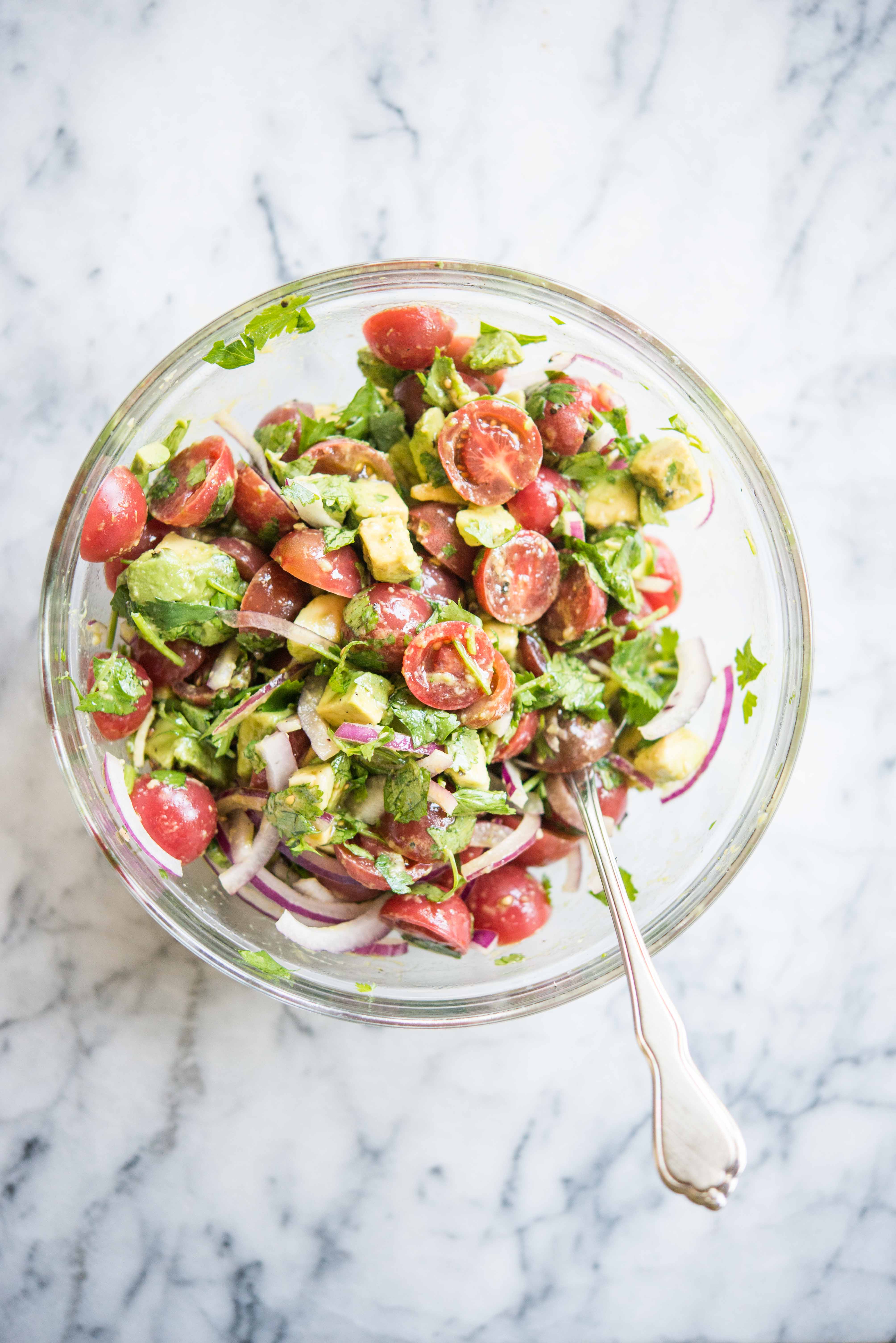 tomatoes, diced avocado, sliced red onion, and cilantro in a glass bowl on a marble countertop