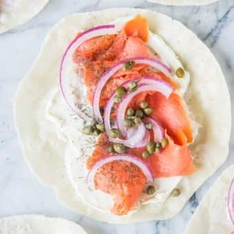 smoked salmon lunch wrap - tortilla smeared with cream cheese, smoked salmon, capers, and red onion, on a marble board