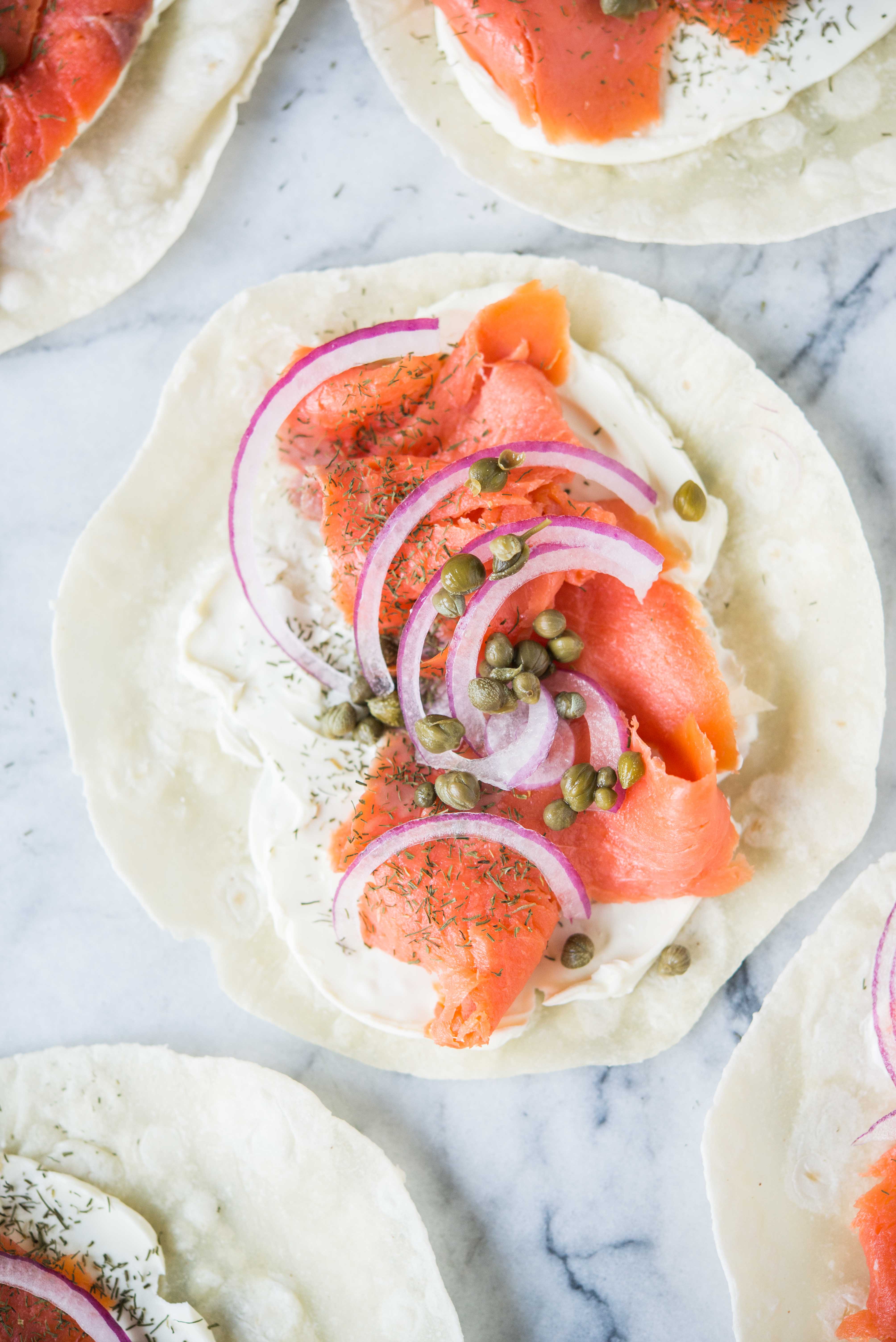 smoked salmon lunch wrap - tortilla smeared with cream cheese, smoked salmon, capers, and red onion, on a marble board