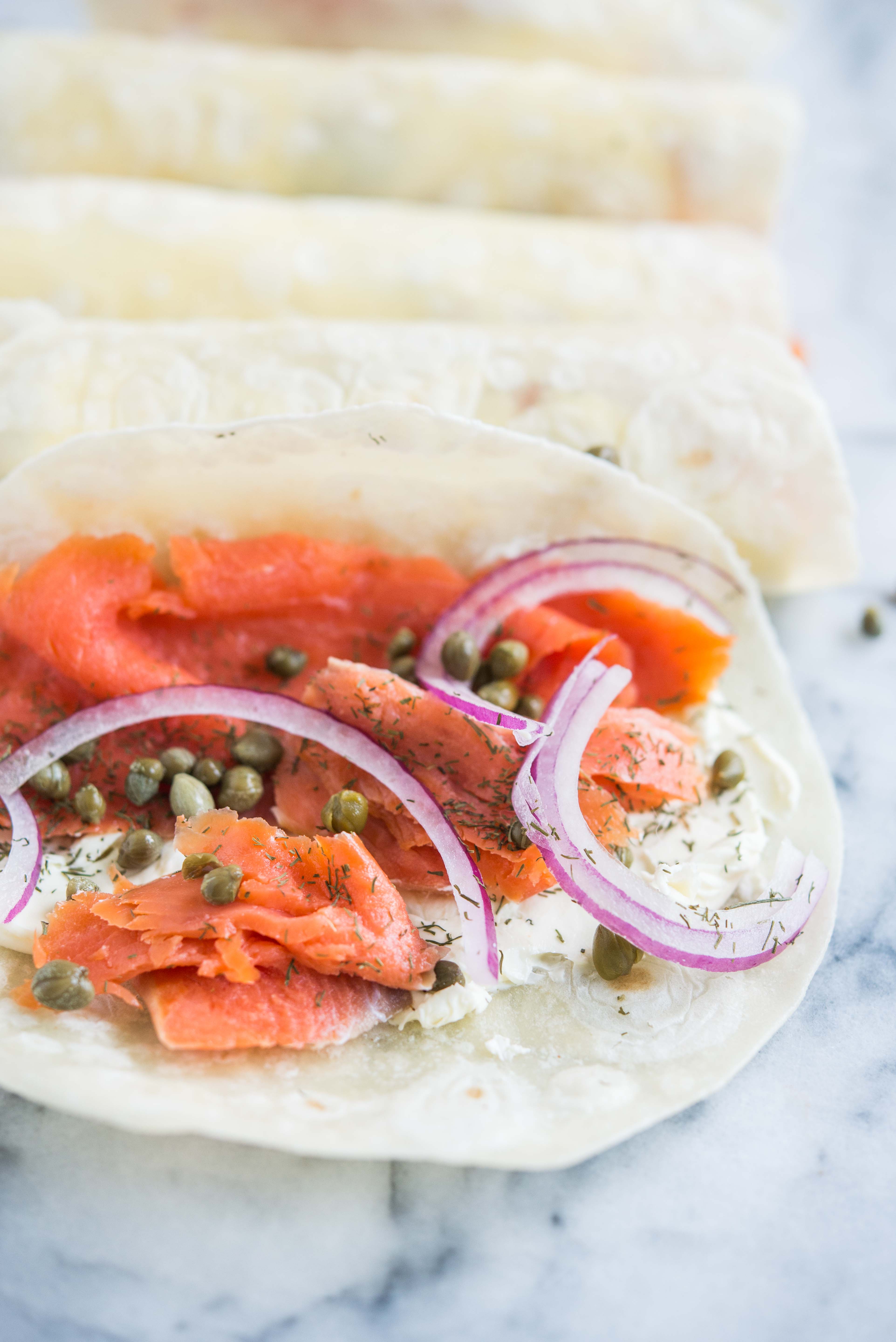 smoked salmon lunch wrap - tortilla smeared with cream cheese, smoked salmon, capers, and red onion, on a marble board