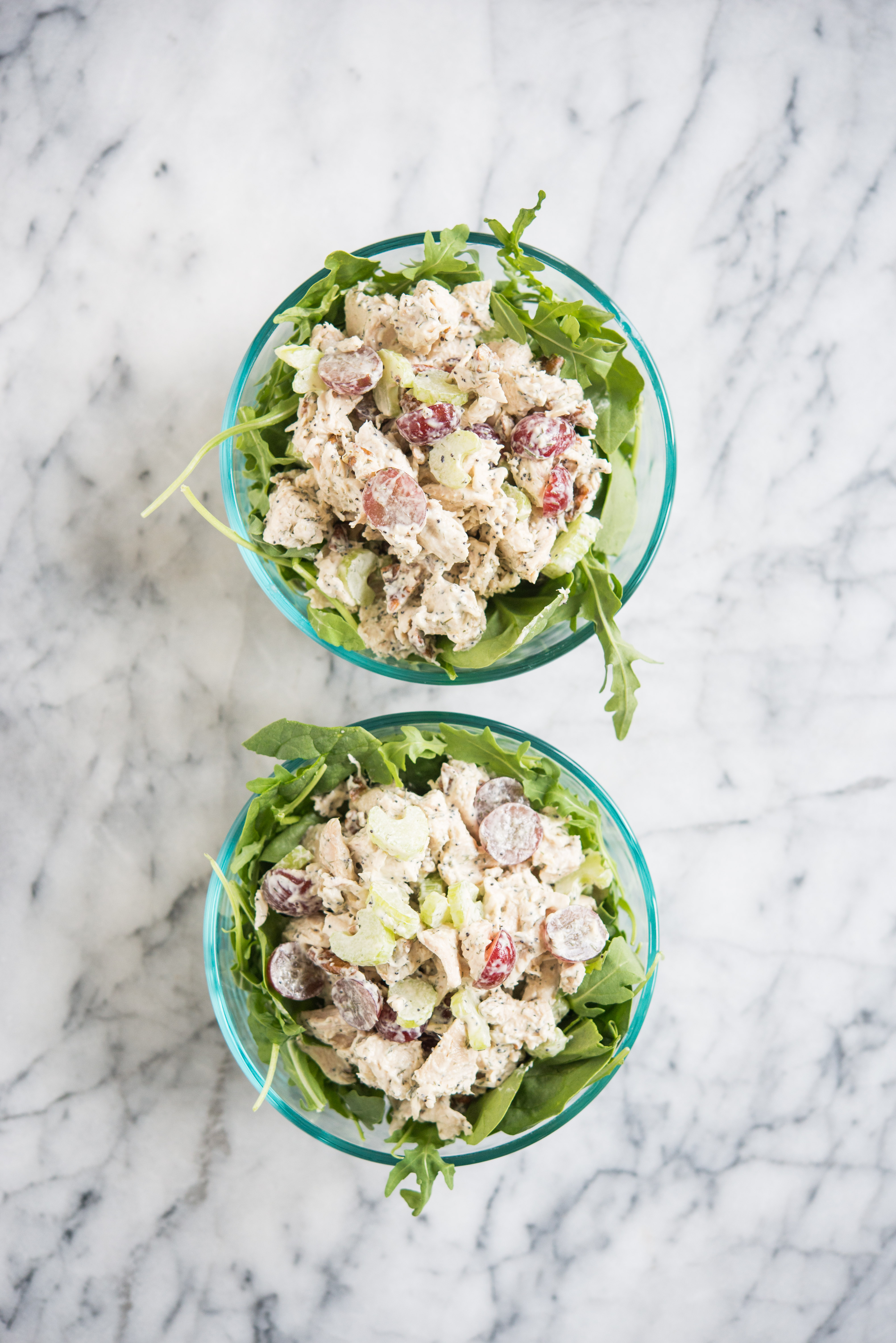 two glass bowls filled with greens topped with chicken salad with grapes and pecans