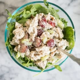 chicken salad with grapes and pecans over mixed greens in a glass bowl on a marble board