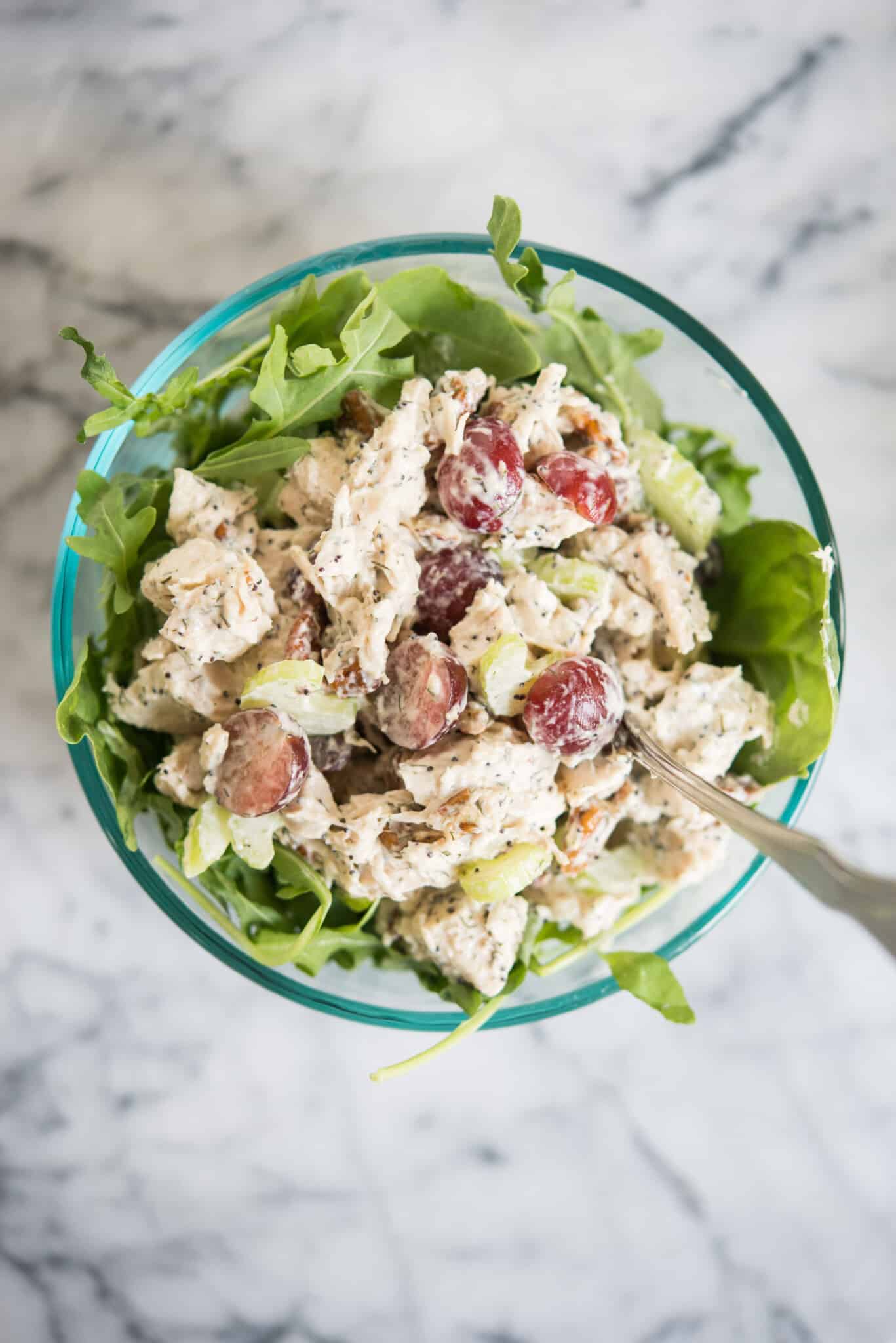 chicken salad with grapes and pecans over mixed greens in a glass bowl on a marble board