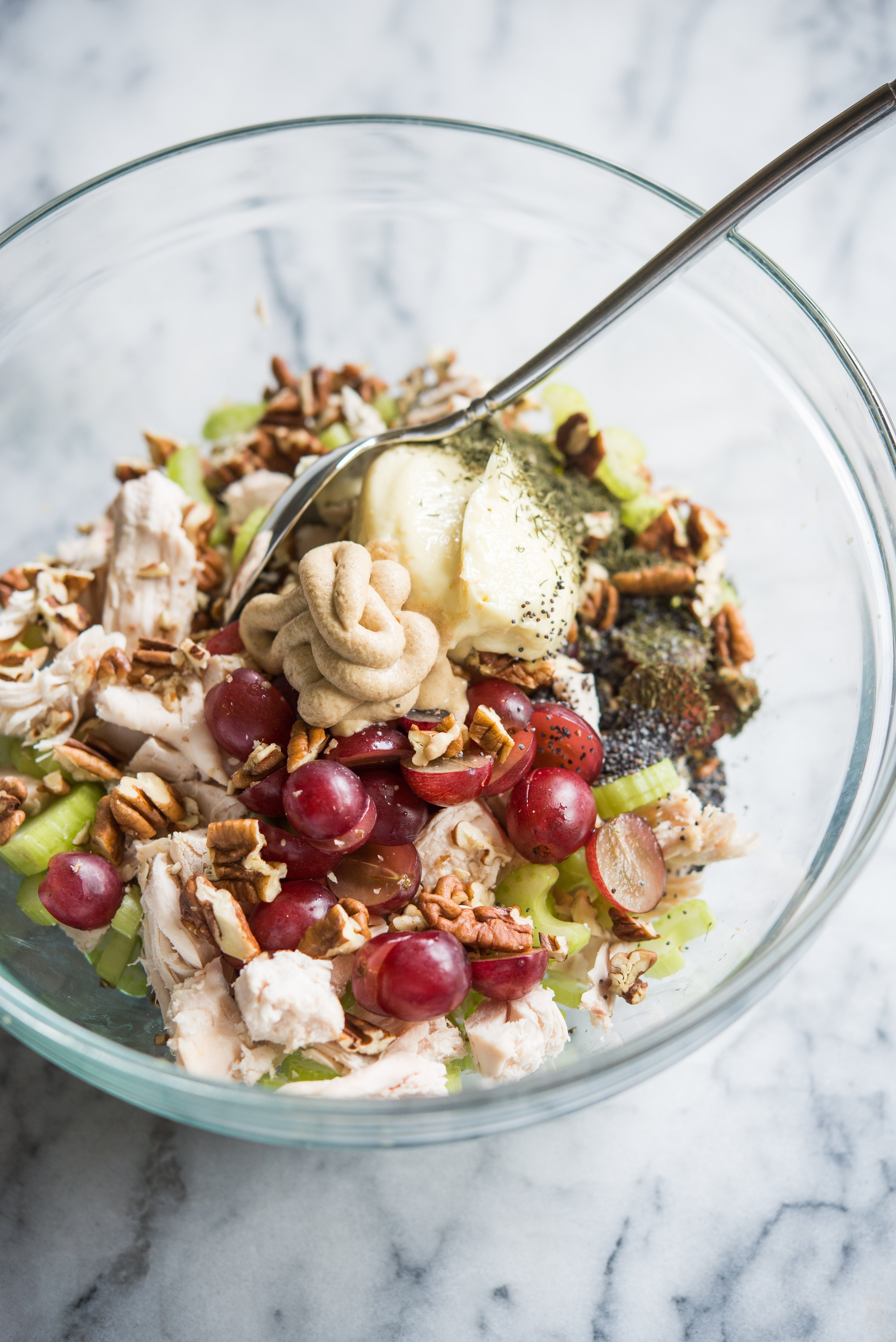 chicken, grapes, pecans, celery, mayo, and mustard in a glass bowl on a marble board