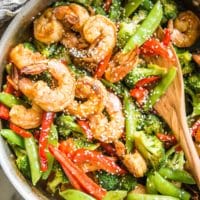 teriyaki shrimp, bell peppers, broccoli, and snow peas in a stainless steel skillet on a marble board