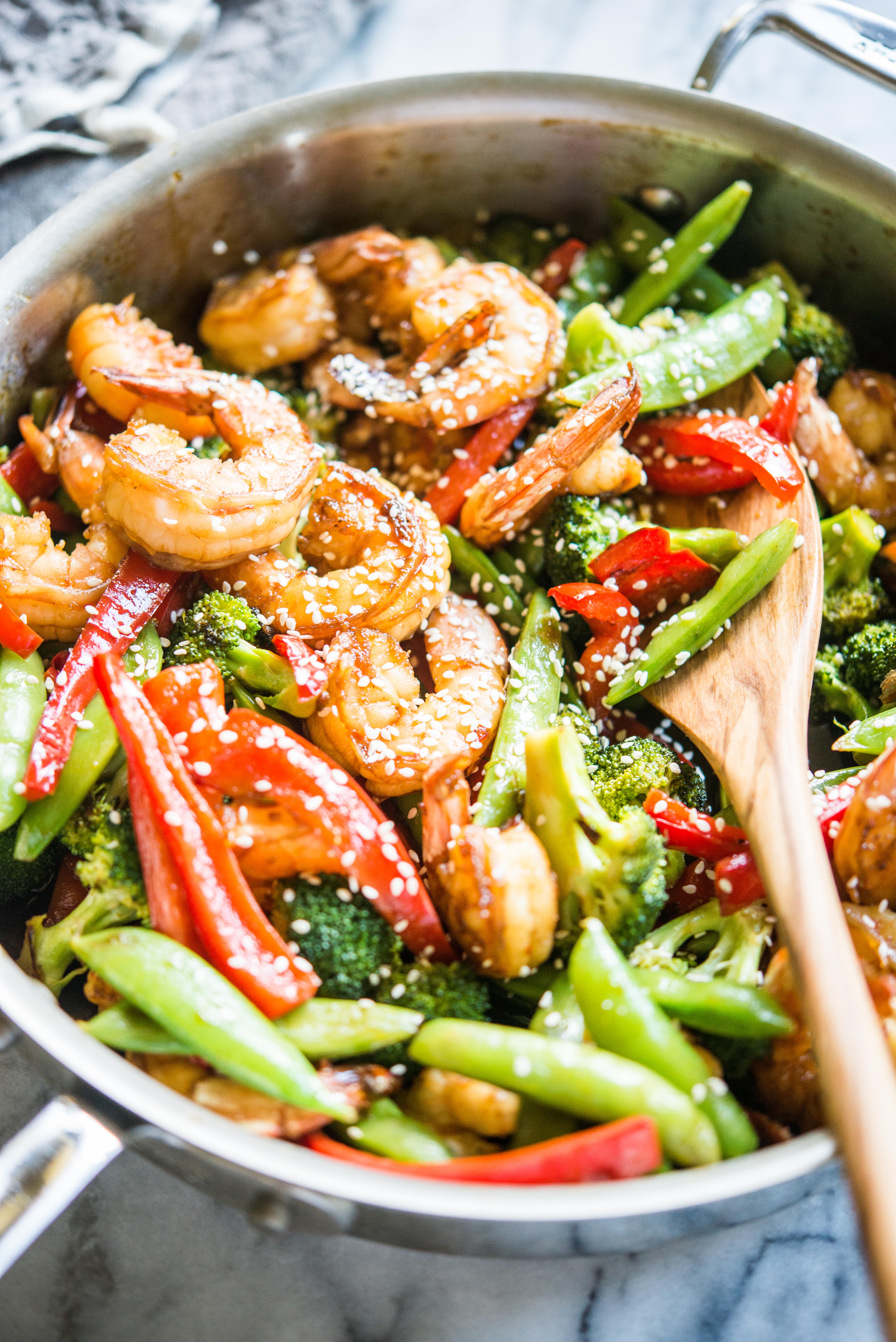 teriyaki shrimp stir fry with shrimp, red bell peppers, broccoli, and snap peas in a stainless steel skillet on a marble countertop