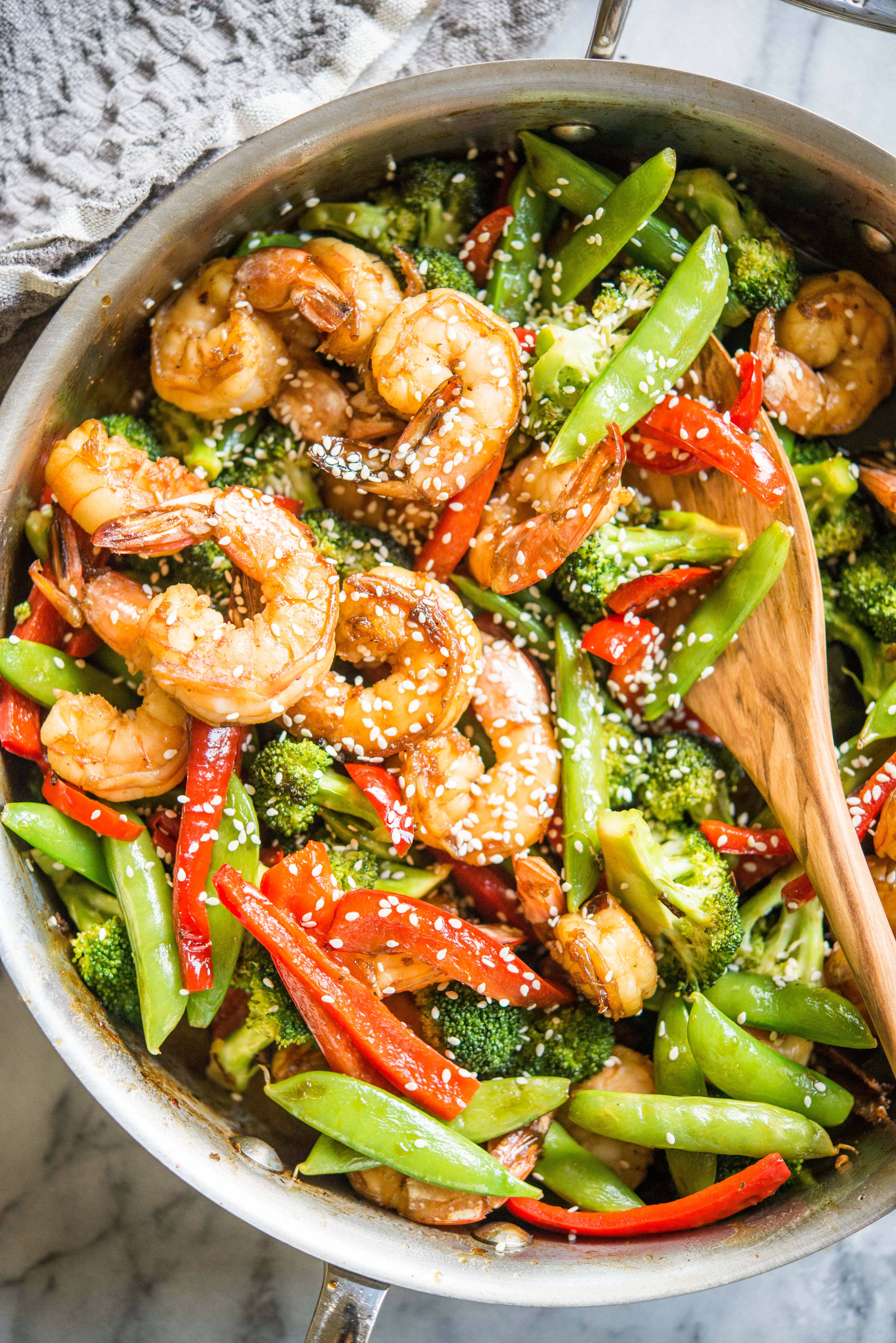 teriyaki shrimp, bell peppers, broccoli, and snow peas in a stainless steel skillet on a marble board