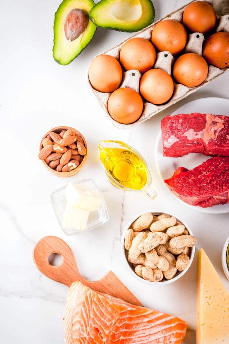 avocados, eggs, beef, salmon, nuts, and oil on a marble board