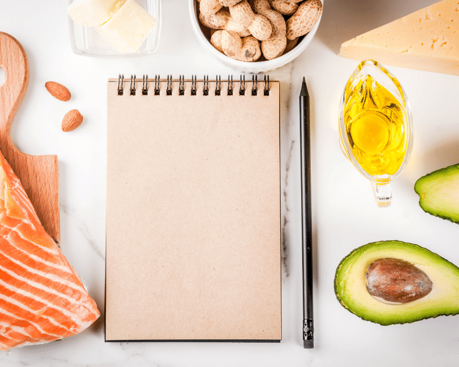 notebook, pen, avocado, oil, peanuts, and salmon on a marble board