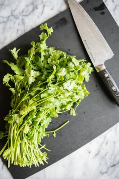 bunch of cilantro on a black cutting board next to a large knife